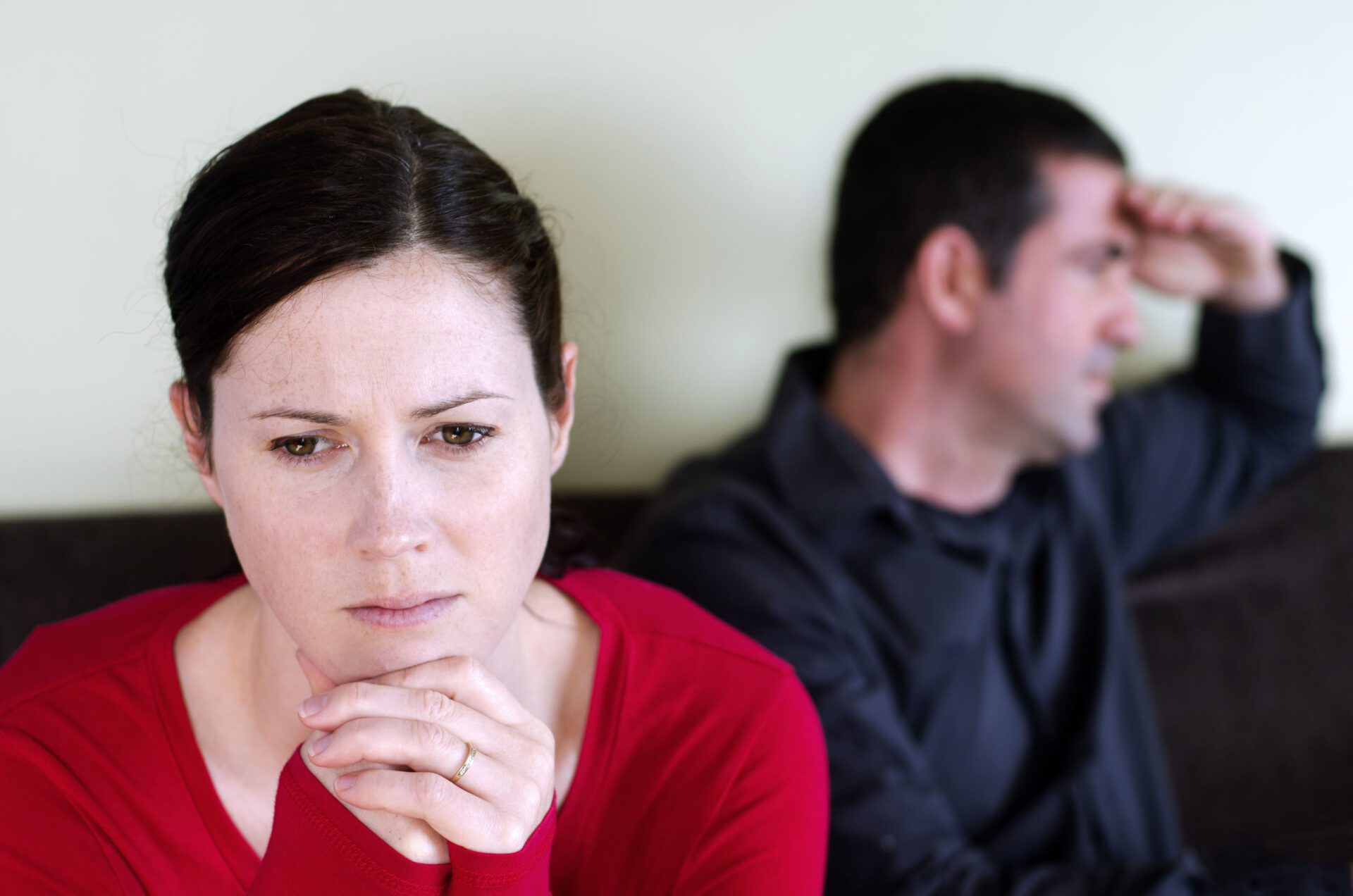 Portrait of unhappy young couple who have fallen out over a disagreement sitting on a sofa. Woman in the front and the man in the background.